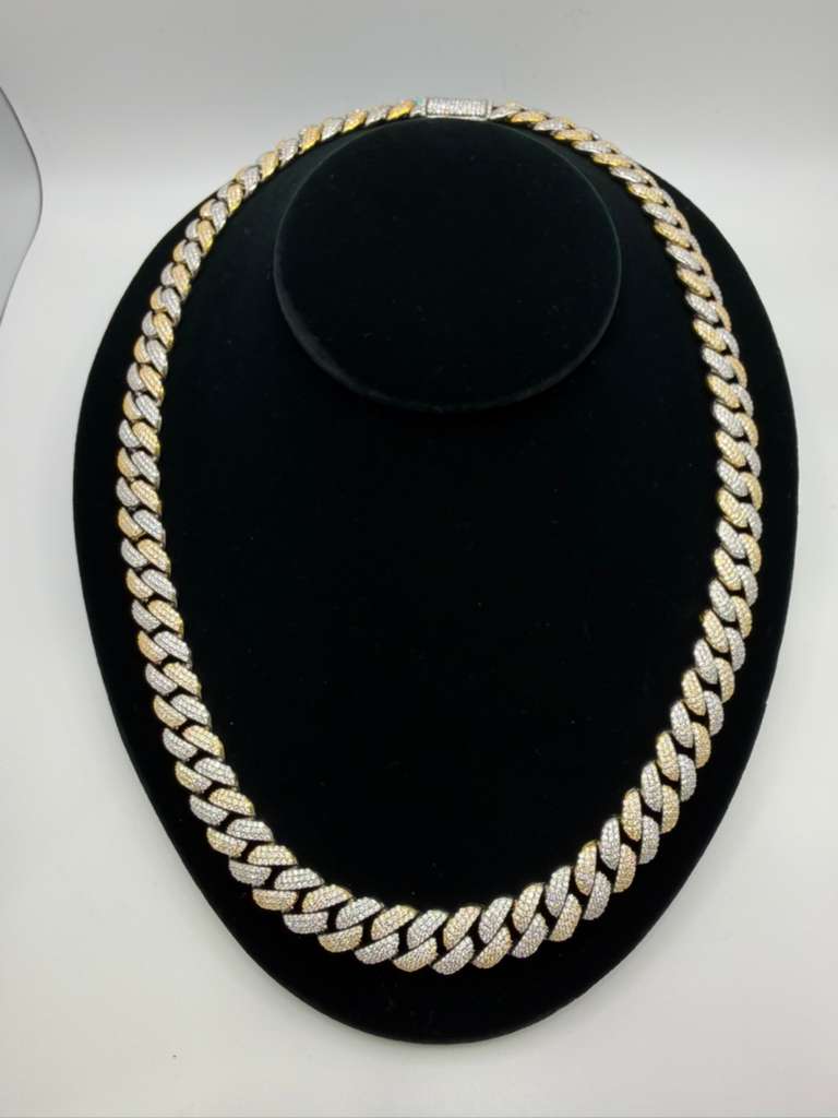 Gold chain necklace on a black stand with a white background